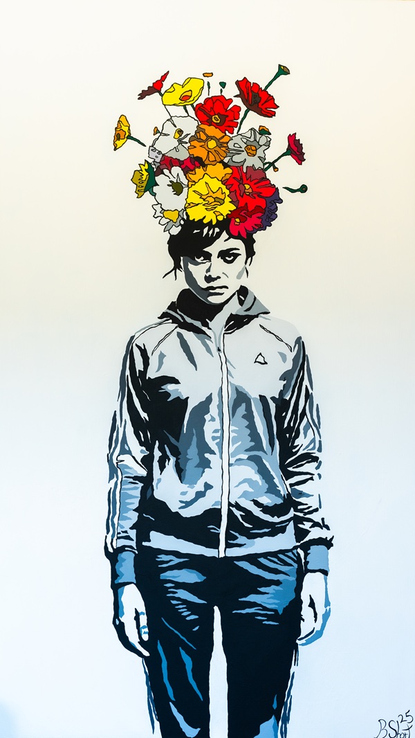 Ein Porträt eines Mädchens in einem grauen Sweatshirt mit bunten Blumen, die aus ihrem Kopf wachsen, vor einem weißen Hintergrund.